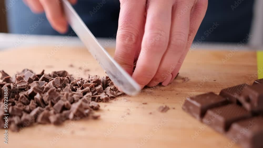 Woman Chopping Black Dark Chocolate on wooden cutting board Woman Chopping Black Dark Chocolate on wooden cutting board