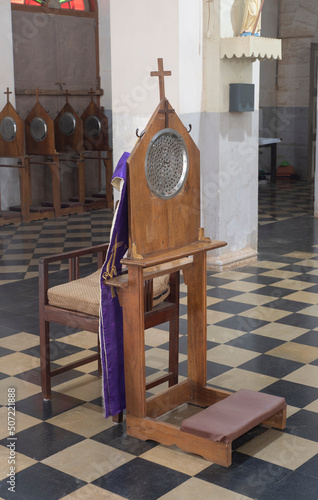 Verical view of a confessional chair and kneeler bench inside a church in southern India. photo