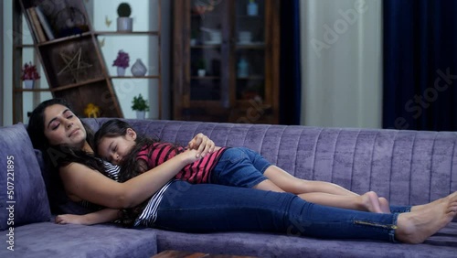 An Indian housewife and her little daughter resting together on a comfortable sofa - mother-daughter bonding  a short nap. An adorable little girl falls asleep in her mother's arms in the living ro... photo