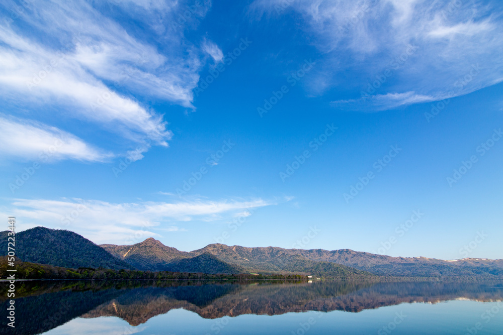 青空の下、山々を湖面に映す湖。北海道の屈斜路湖。