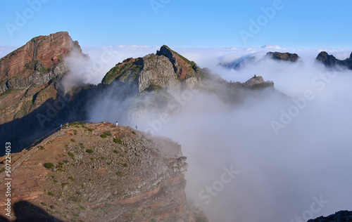 Panorama from Pico do Areeiro  a starting point of PR1 hiking trail in the Madeira Island. Hikers on the trail to the Pico Ruivo. Fog ascending from a valley and remaining among mountain folds.
