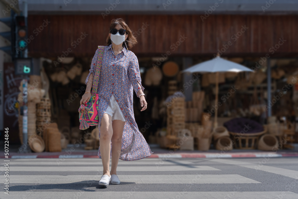 Fototapeta premium Tourist Asian woman walks across the street in front of an old storefront famous wicker ware shop in downtown famous places Chang Moi Road, Chiang Mai, Northern Thailand.