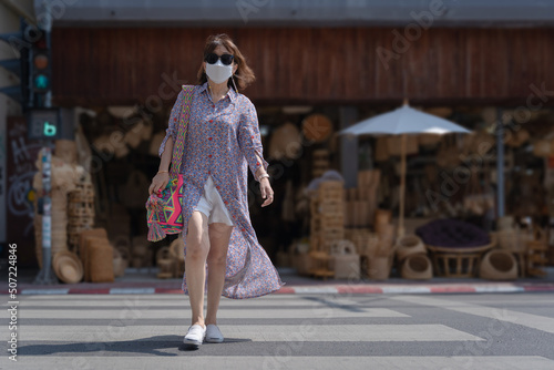 Tourist Asian woman walks across the street in front of an old storefront famous wicker ware shop in downtown famous places Chang Moi Road, Chiang Mai, Northern Thailand.