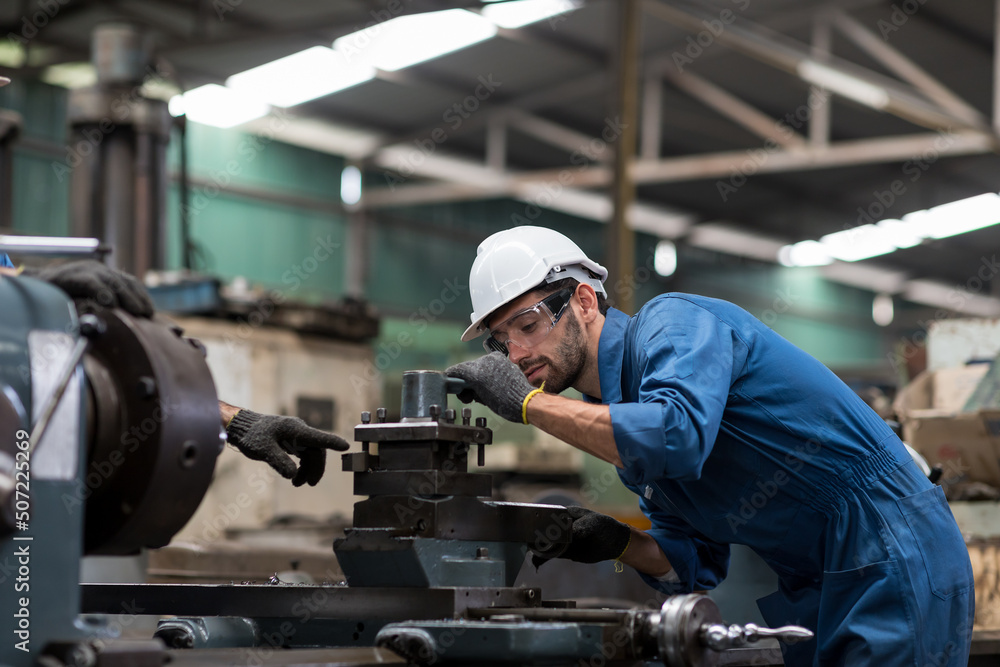 Engineer male worker in white hard hat working with production machinery in the factory. Factory worker maintaining CNC machine lathe metal at the industry factory. Engineer male worker in white hard hat working with production machinery in the factory. Factory worker maintaining CNC machine lathe metal at the industry factory.