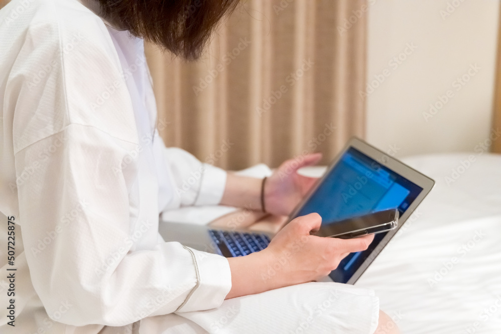 ホテルのベッドでリモートワークしている女性　ワーケーション　出張　イメージ