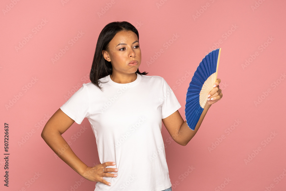 African american tired overheated woman using paper fan suffer from heat sweating, cools herself, feels sluggish due problem no air conditioner at home at summer weather, isolated on pink background African american tired overheated woman using paper fan suffer from heat sweating, cools herself, feels sluggish due problem no air conditioner at home at summer weather, isolated on pink background
