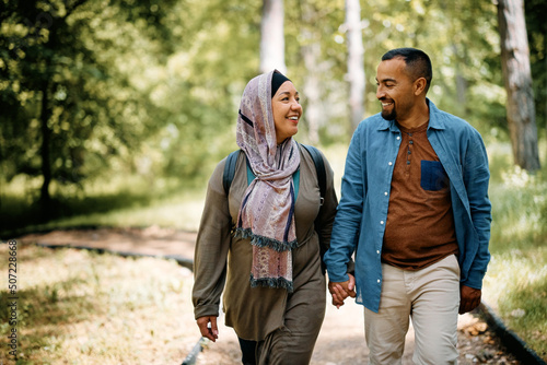 Happy Middle Eastern couple holding hands while walking through park. © Drazen