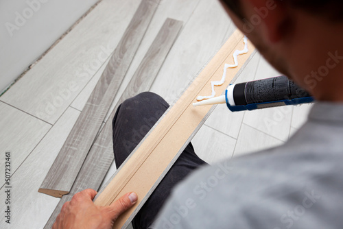 Foto A worker applies glue to a baseboard before installing it on the floor