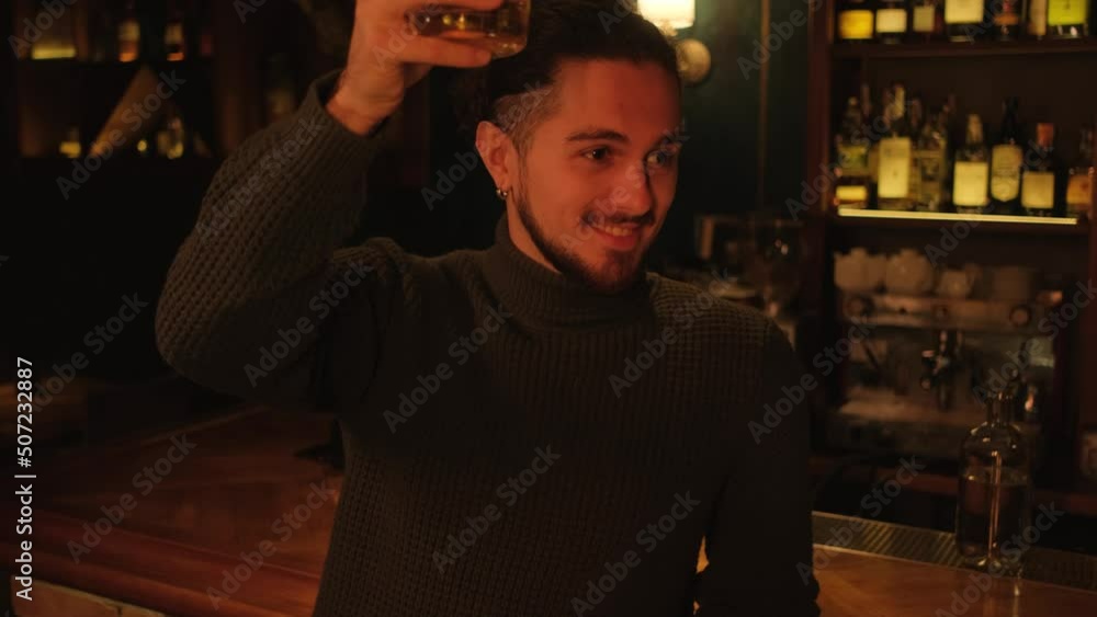 A young man in a dark bar raises a glass with an alcoholic drink and has fun. Rest after a working day. A young man in a dark bar raises a glass with an alcoholic drink and has fun. Rest after a working day.