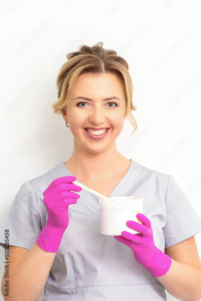 Portrait of a female caucasian beautician holding a jar of sugar paste for sugaring wearing pink gloves on white background Portrait of a female caucasian beautician holding a jar of sugar paste for sugaring wearing pink gloves on white background