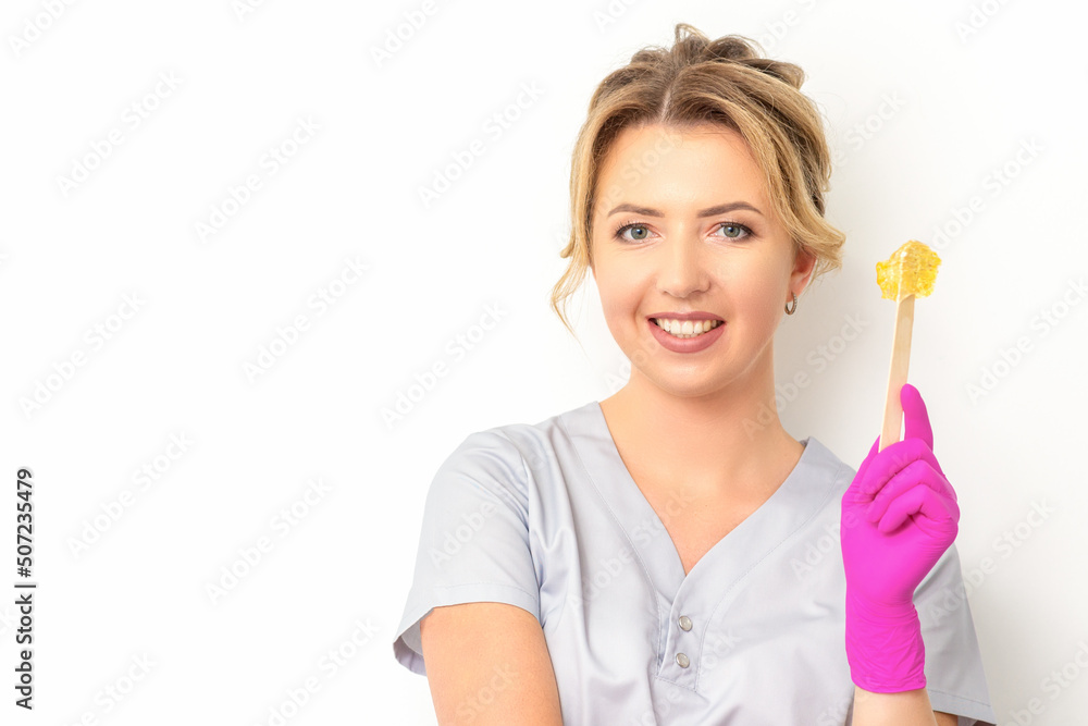 The master of sugar hair removal holds liquid yellow sugar paste, wax for depilation on a wooden stick on a white background The master of sugar hair removal holds liquid yellow sugar paste, wax for depilation on a wooden stick on a white background