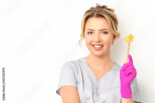 The master of sugar hair removal holds liquid yellow sugar paste, wax for depilation on a wooden stick on a white background