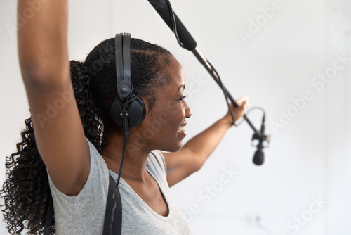 Video Production Crew Member African American Woman Smiling Working on Set as Audio Person Holding Boom Pole Microphone Recording Audio 