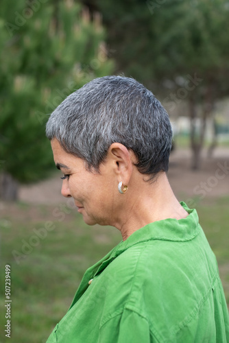 Side view of attractive woman with grey hair in park. Female model with short grey hair in bright clothes looking at camera. Beauty, portrait concept