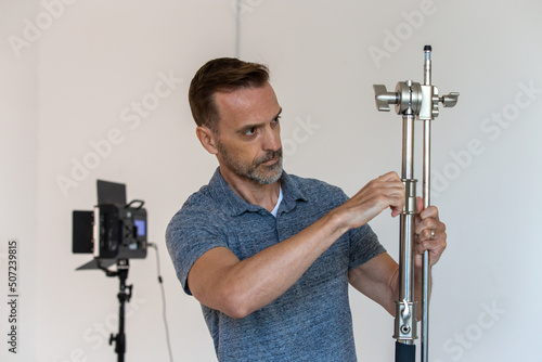 Behind the Scenes of a Caucasian Man Setting Up C-stand on a Video Production or Movie Set. Gaffer Works as a Crew Member in the Film Industry