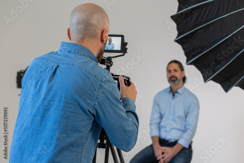Videographer or Camera Man is Filming Male in Front of Camera And Lighting. Behind the Scenes on Corporate Video Production Set. 