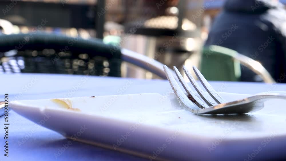 Empty plate with food leftovers immediately after eating on the patio of a bar, fork still on the plate, close up view macro shot outdoors. Empty plate with food leftovers immediately after eating on the patio of a bar, fork still on the plate, close up view macro shot outdoors.