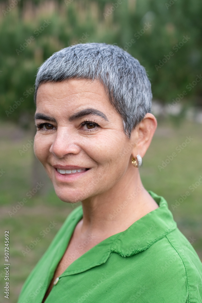 Portrait of smiling woman with grey hair in park. Female model with short grey hair in bright clothes looking at camera. Beauty, portrait concept Portrait of smiling woman with grey hair in park. Female model with short grey hair in bright clothes looking at camera. Beauty, portrait concept
