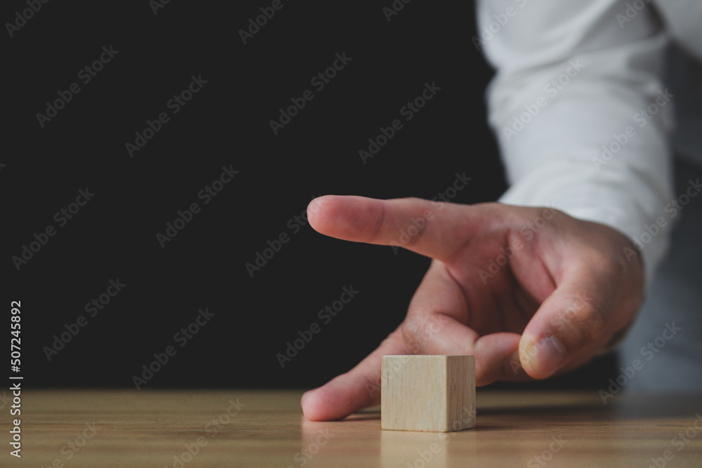 Someone uses fingers to flick a wood block. In the business, it shows a selling or cutting of some business to stop loss. Strategy Idea. This close up shot with some slightly focus.