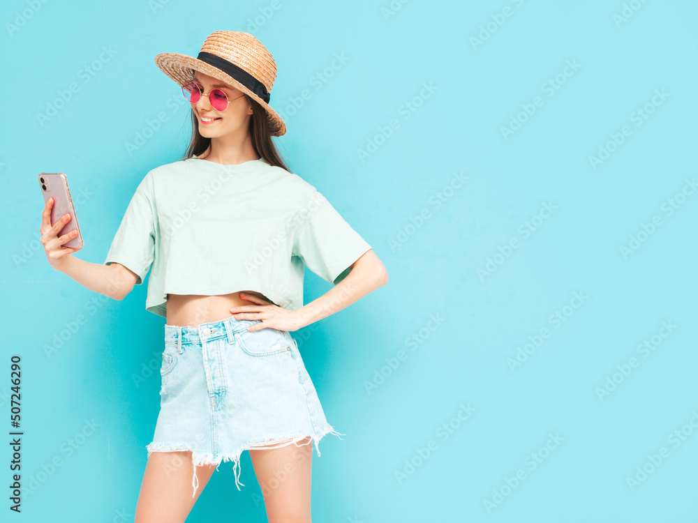 Young beautiful smiling female in trendy summer skirt. Sexy woman with posing near yellow wall in studio. Positive model having fun. In sunglasses and hat.Looking at smartphone. Using apps Young beautiful smiling female in trendy summer skirt. Sexy woman with posing near yellow wall in studio. Positive model having fun. In sunglasses and hat.Looking at smartphone. Using apps