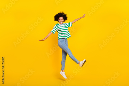 Full body photo of funky millennial lady jump wear t-shirt jeans footwear isolated on yellow color background