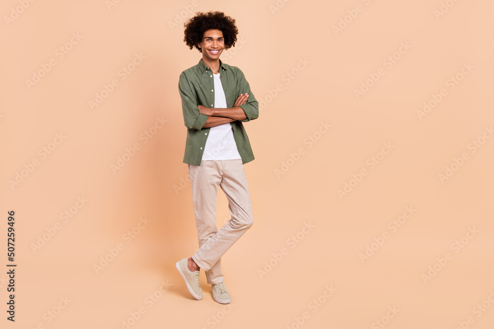 Full length body size view of attractive cheerful content wavy-haired guy folded arms isolated over beige pastel color background Full length body size view of attractive cheerful content wavy-haired guy folded arms isolated over beige pastel color background