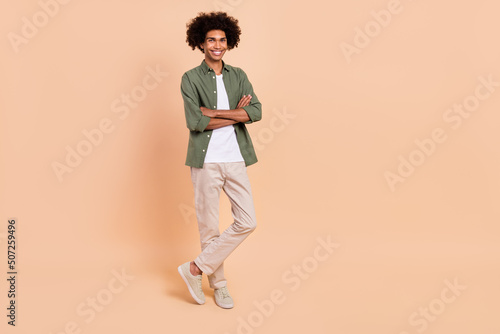 Full length body size view of attractive cheerful content wavy-haired guy folded arms isolated over beige pastel color background