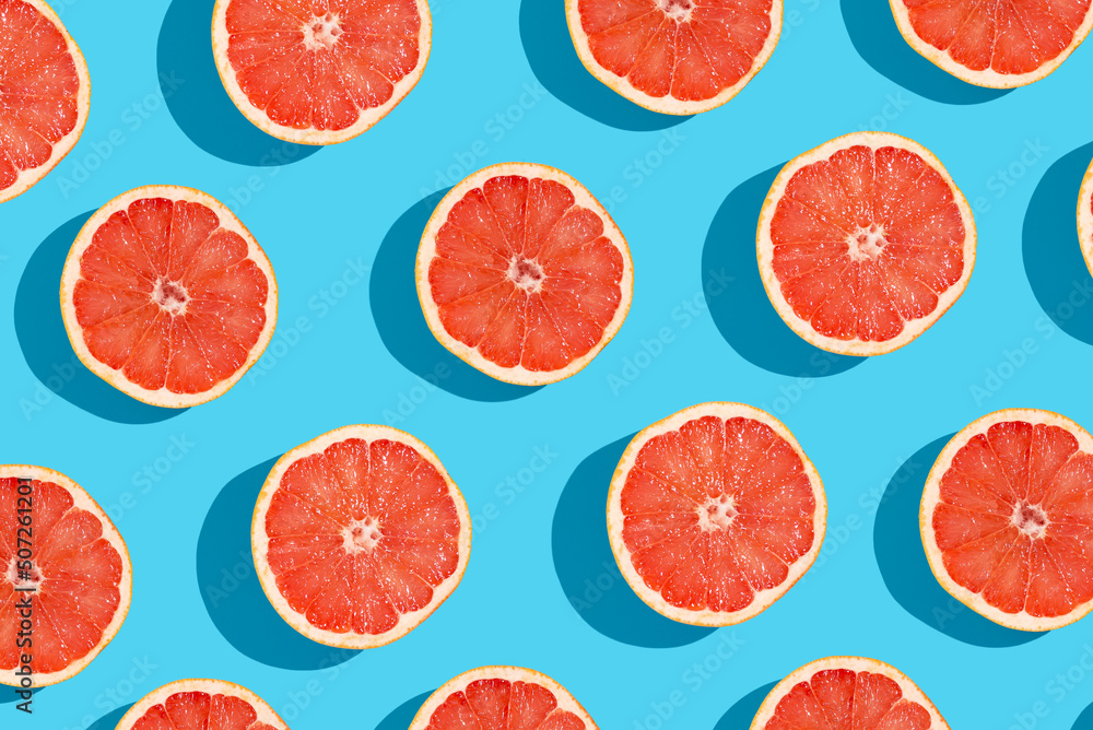 Many fresh slices of grapefruits on blue background, flat lay. Pattern design