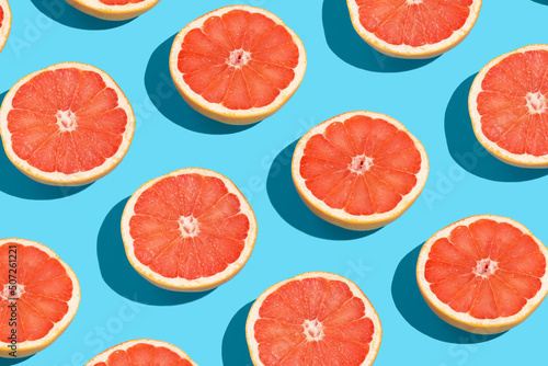Many fresh slices of grapefruits on blue background, flat lay. Pattern design