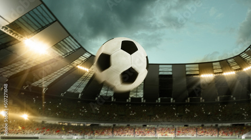 Flight of soccer football ball through crowded stadium with spotlights in evening time. Concept of sport, art, energy, power. Unfocus effect