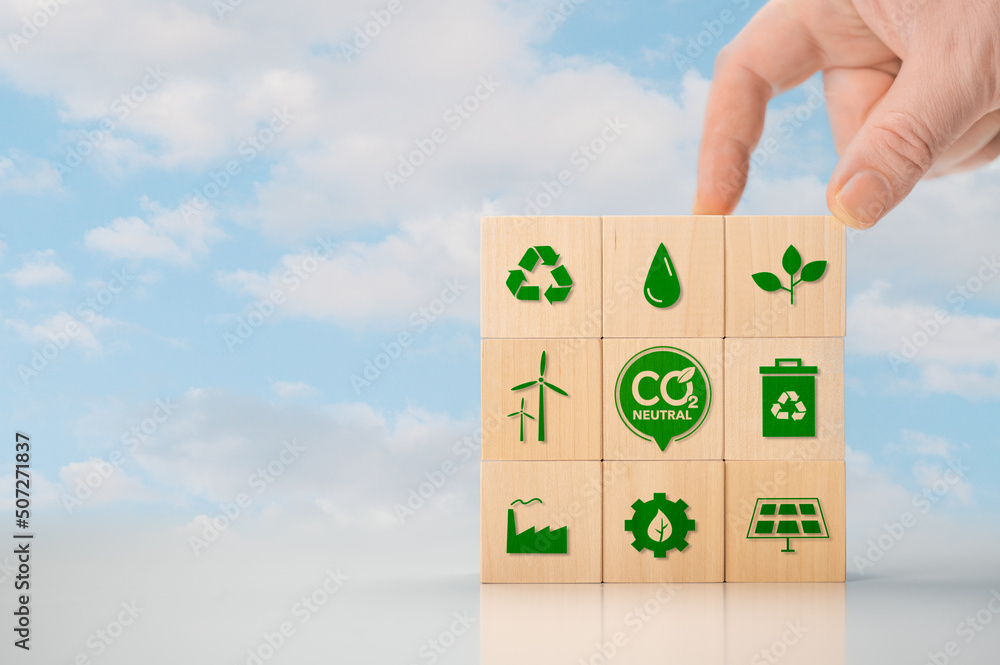 Climate neutral long term strategy. Hand put wooden cubes with green icon and green icon on blue background. Climate neutral long term strategy. Wooden cube with carbon neutral, green factory icon. Climate neutral long term strategy. Hand put wooden cubes with green icon and green icon on blue background. Climate neutral long term strategy. Wooden cube with carbon neutral, green factory icon.