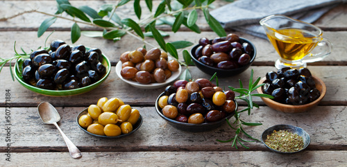 Assorted olives on a plate with olive tree brunches. Wooden table background. Close up.