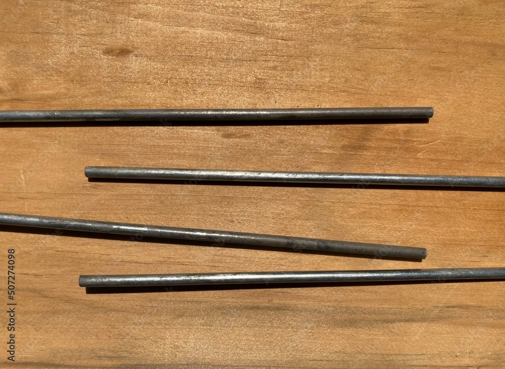 metal rods lie arranged on a light brown wood surface metal rods lie arranged on a light brown wood surface