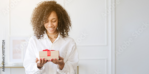 Excited african American young woman unpack gift box, overjoyed girl feel euphoric open shipped package parcel from delivery service                               