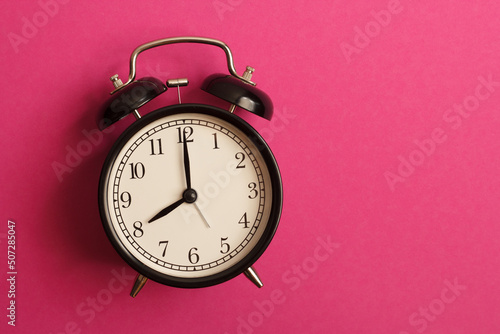 black vintage style alarm clock isolated on a pink background