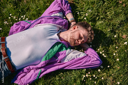 Young blond man lying on a green meadow with a relaxed expression on his face