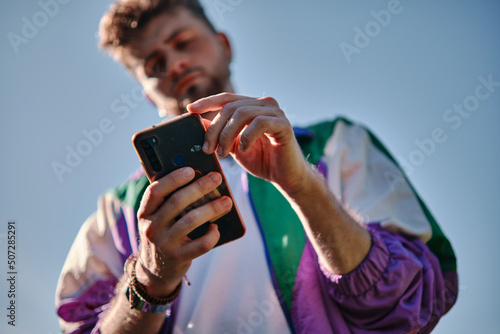 Young man looking at his mobile phone seen from below, focusing on the phone