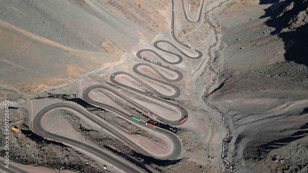 Aerial orbit of the Cuesta Caracoles road, border between Chile and Argentina, cargo trucks passing through the curves, sunny day. Aerial orbit of the Cuesta Caracoles road, border between Chile and Argentina, cargo trucks passing through the curves, sunny day.