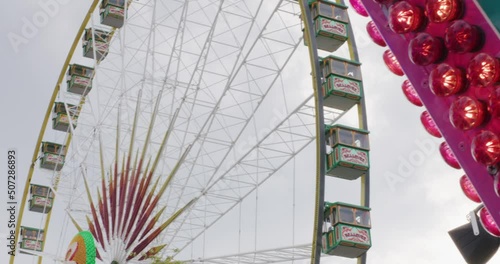 People riding inside on a ferris wheel next to red sign at Balvarian festival at Stuttgart, Germany, Europe at sunset, panning view angle photo