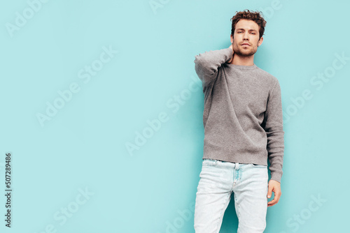 Portrait of handsome confident  model. Sexy stylish man dressed in  sweater and jeans. Fashion hipster male with curly hairstyle posing near blue wall in studio. Isolated © halayalex