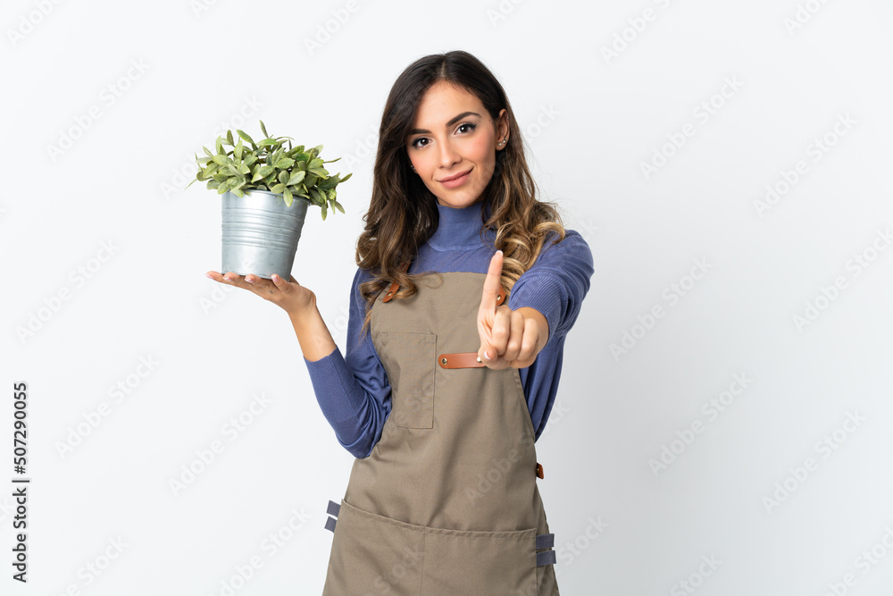 Gardener girl holding a plant isolated on white background showing and lifting a finger Gardener girl holding a plant isolated on white background showing and lifting a finger