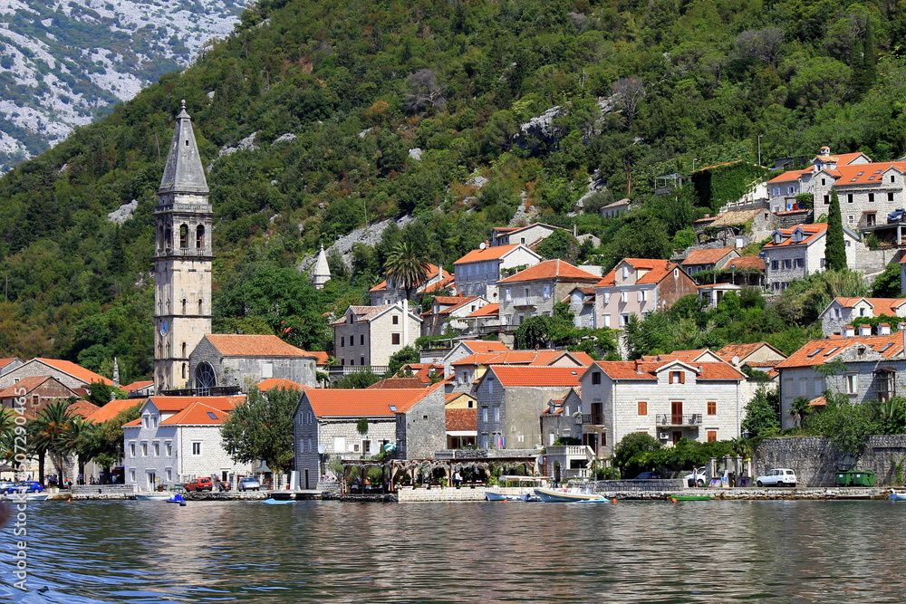 small town, old houses with red roofs on shore of Kotor Bay among high mountains in Montenegro. Tourism, sea holidays, travel in Montenegro