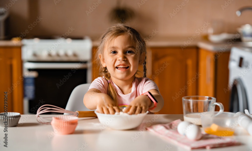 Cute smiling little blonde girl cooking dough in kitchen at home Cute smiling little blonde girl cooking dough in kitchen at home