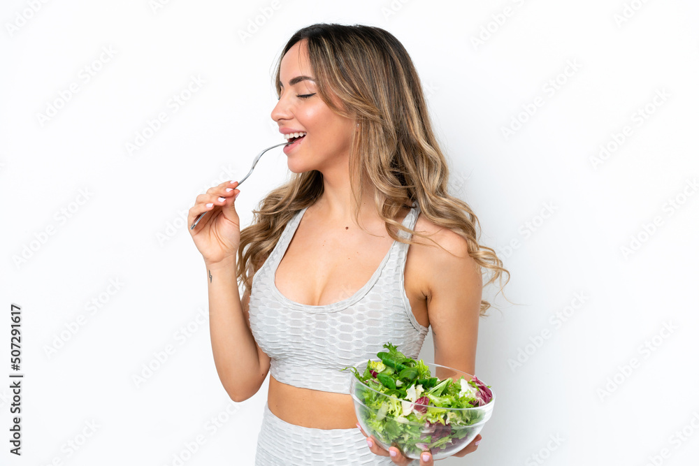 Young caucasian woman isolated on white background holding a bowl of salad and looking at it with happy expression Young caucasian woman isolated on white background holding a bowl of salad and looking at it with happy expression