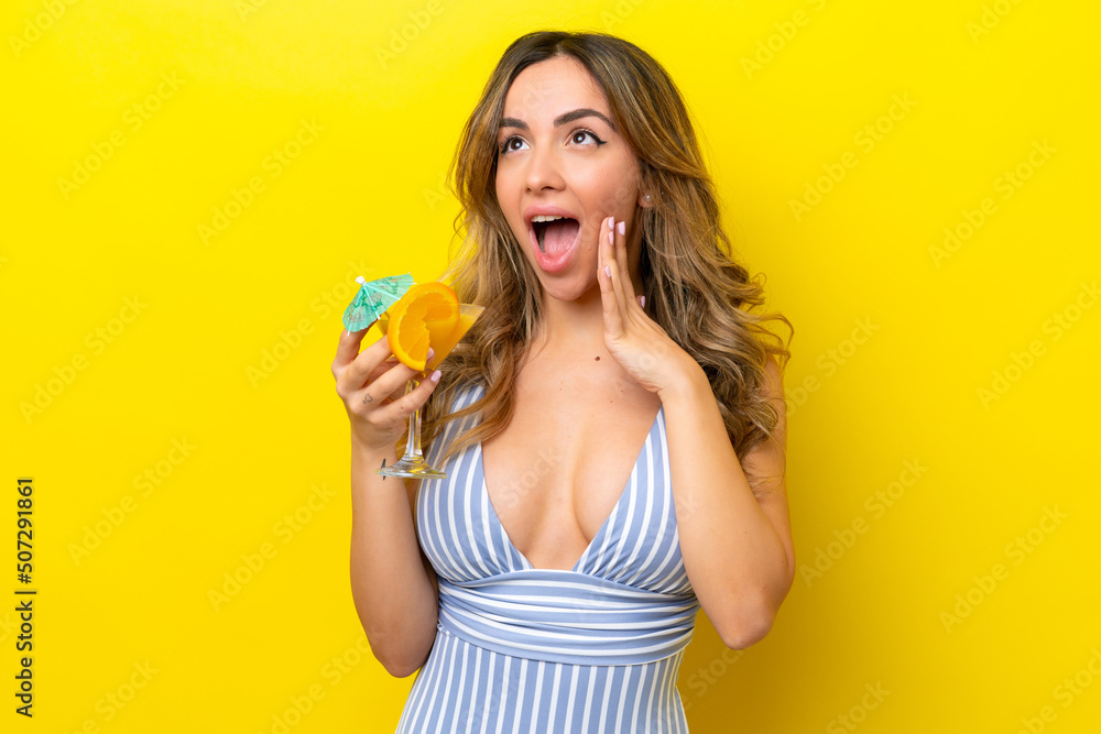 Young caucasian woman isolated on yellow background in swimsuit and holding a cocktail Young caucasian woman isolated on yellow background in swimsuit and holding a cocktail