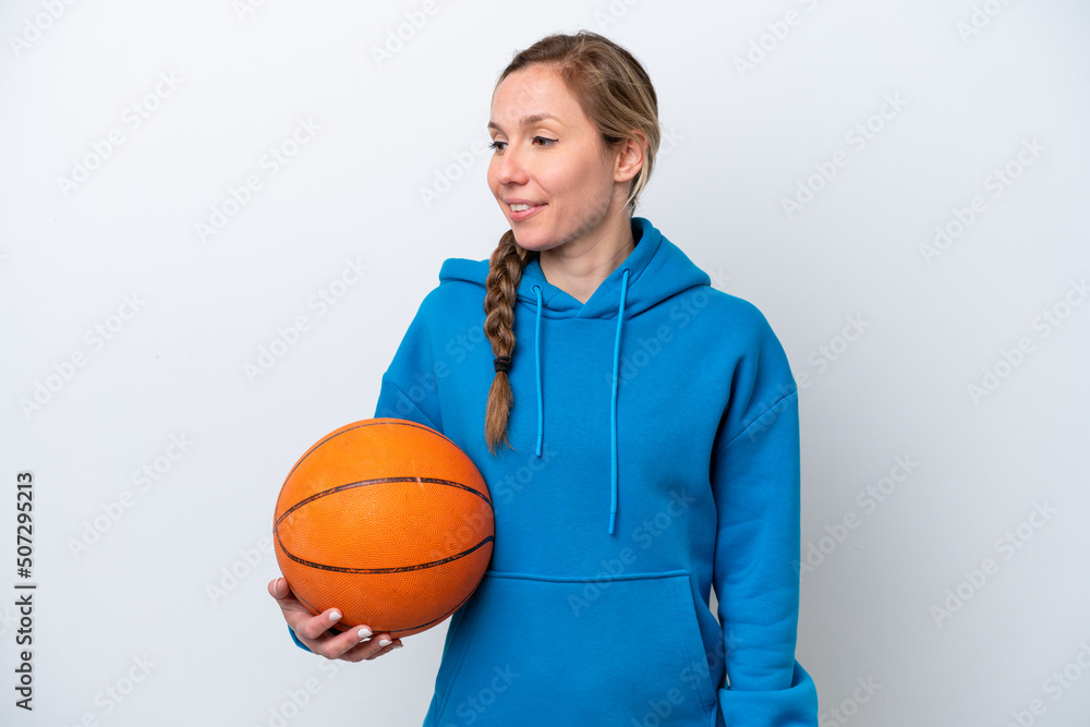 Young caucasian woman playing basketball isolated on white background looking to the side and smiling