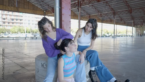 Roller skater girls in colorful clothes sit outdoors and fix hair photo