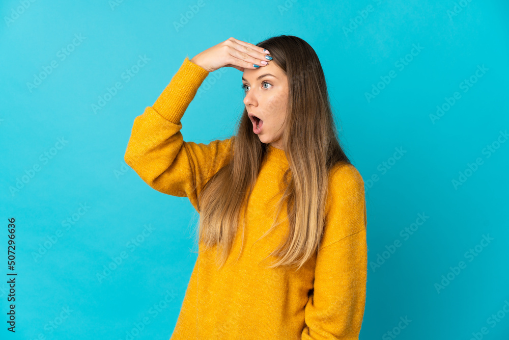 Young Lithuanian woman isolated on blue background doing surprise gesture while looking to the side Young Lithuanian woman isolated on blue background doing surprise gesture while looking to the side