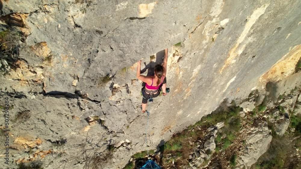 AERIAL: Top view of sporty woman lead climbing and using quickdraw for safety. Female rock climber on her way up the wall hooking the rope. Adrenaline sport activities in beautiful outdoor environment AERIAL: Top view of sporty woman lead climbing and using quickdraw for safety. Female rock climber on her way up the wall hooking the rope. Adrenaline sport activities in beautiful outdoor environment