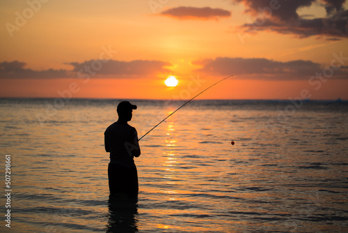 A man fishing in the Indian ocean with the beach at sunset